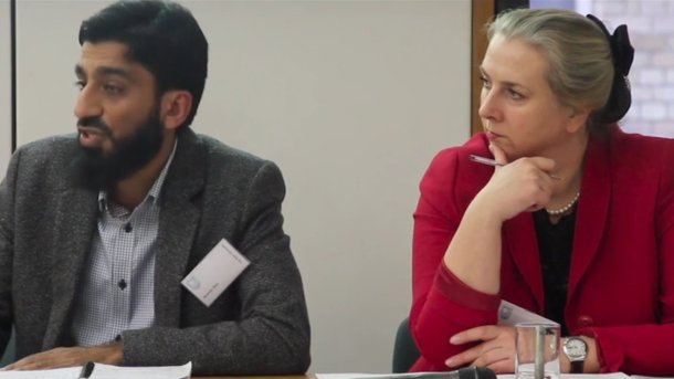 A man and woman sitting next to each other at a table looking off to the left.