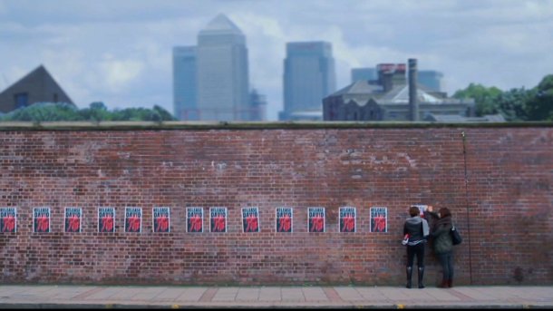 Two girls sticking up posters on a brick wall.